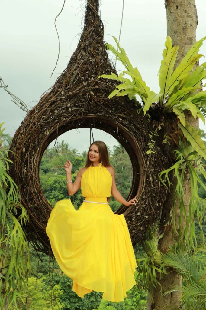 A guest in a yellow dress smiling in the bird nest photo spot at Aloha