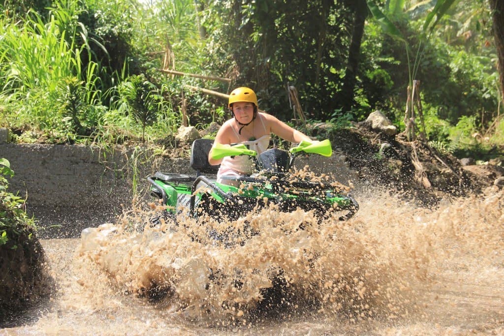A rider on a green quad splashing through a muddy river crossing on the jungle ATV track