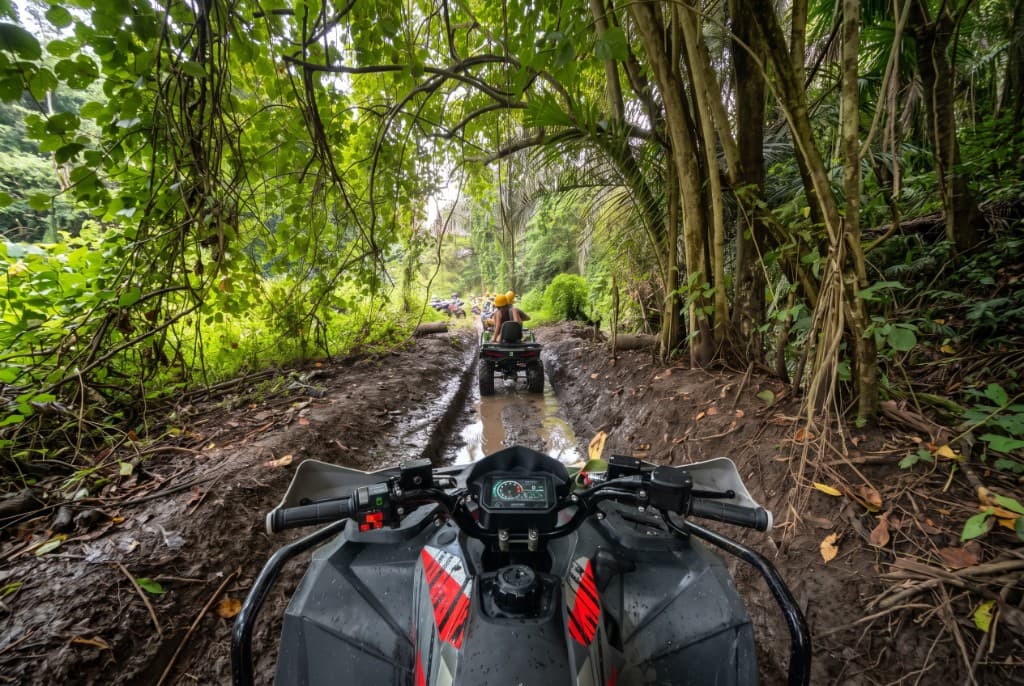 Handlebar view of the muddy Sedang ATV track with deep ruts under the jungle canopy