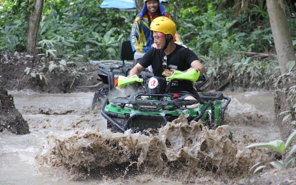 A quad throwing up a wave of muddy water in a river crossing