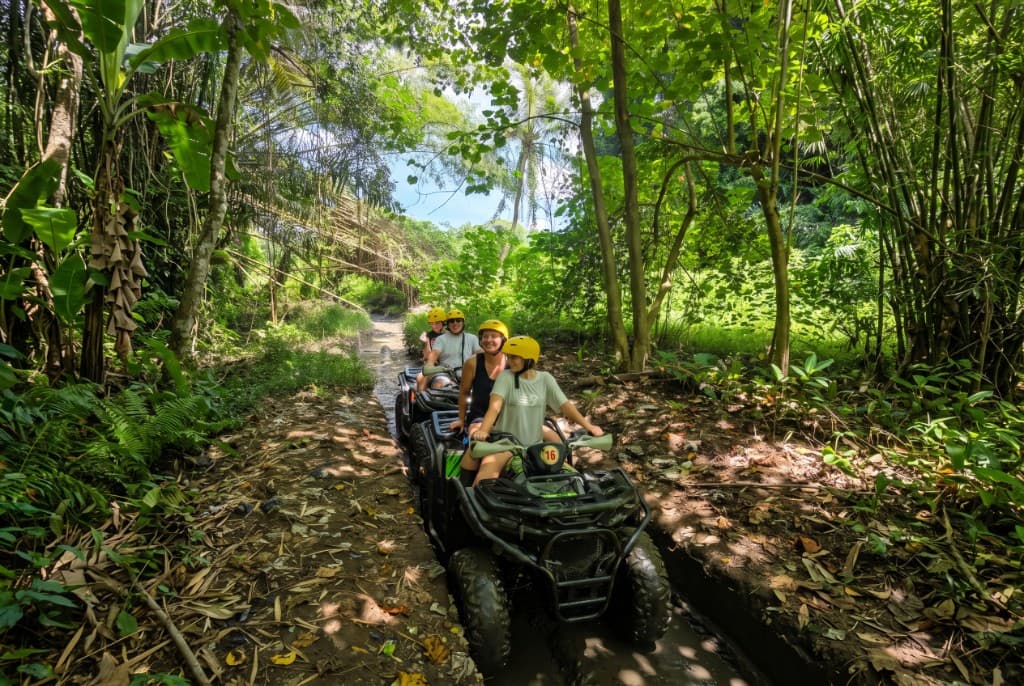 Guests on tandem quads smiling on a narrow muddy jungle track