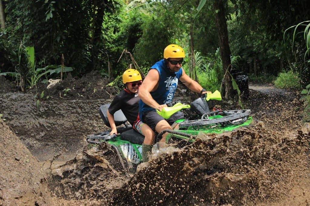 A parent driving a tandem quad through the mud with a child riding behind