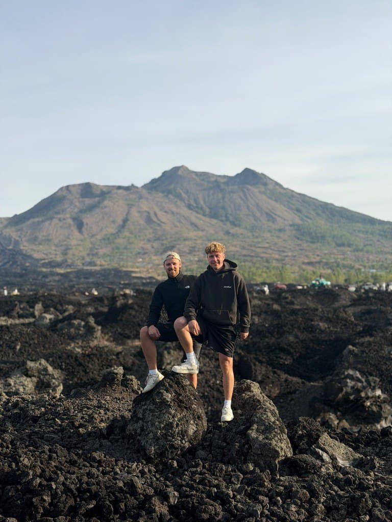 Two guests standing on lava rocks with Mount Batur behind