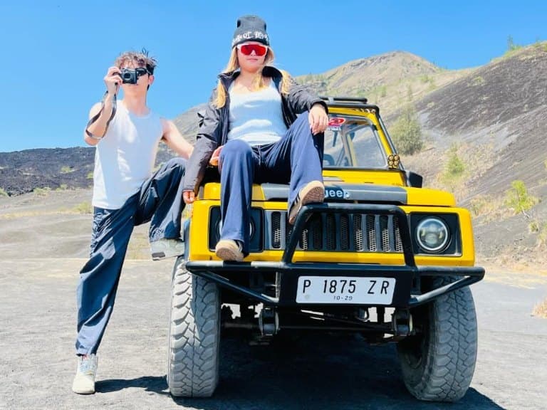 A couple with their yellow jeep on the black sand below Mount Batur