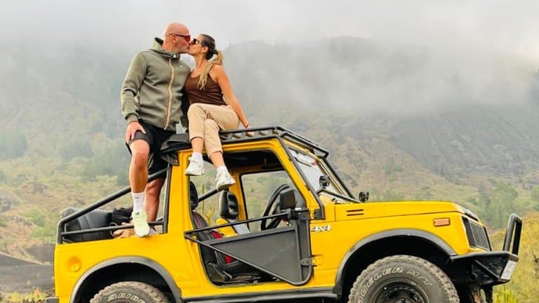 A couple kissing on the roof of a yellow jeep below the misty slopes of Mount Batur