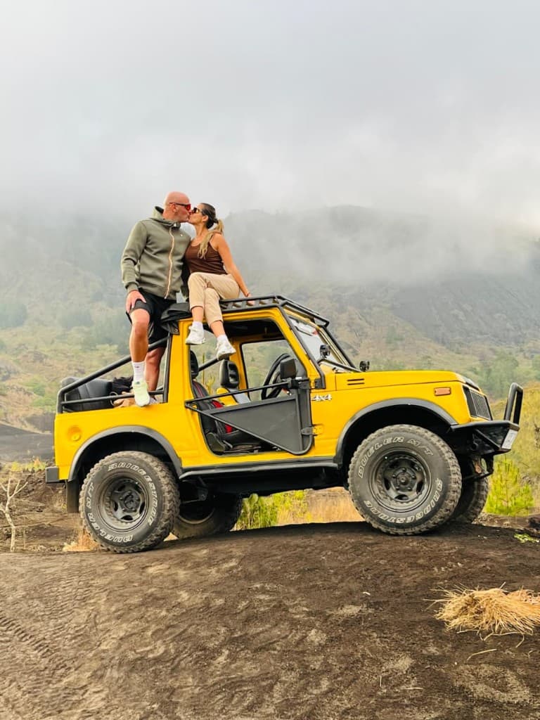 A couple kissing on the roof of a yellow jeep below the misty slopes of Mount Batur