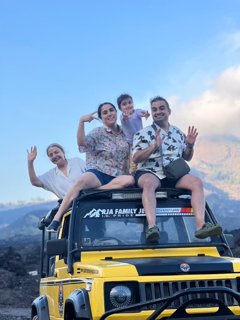 Three generations of a family, including a toddler, waving from a jeep roof above the Batur lava field