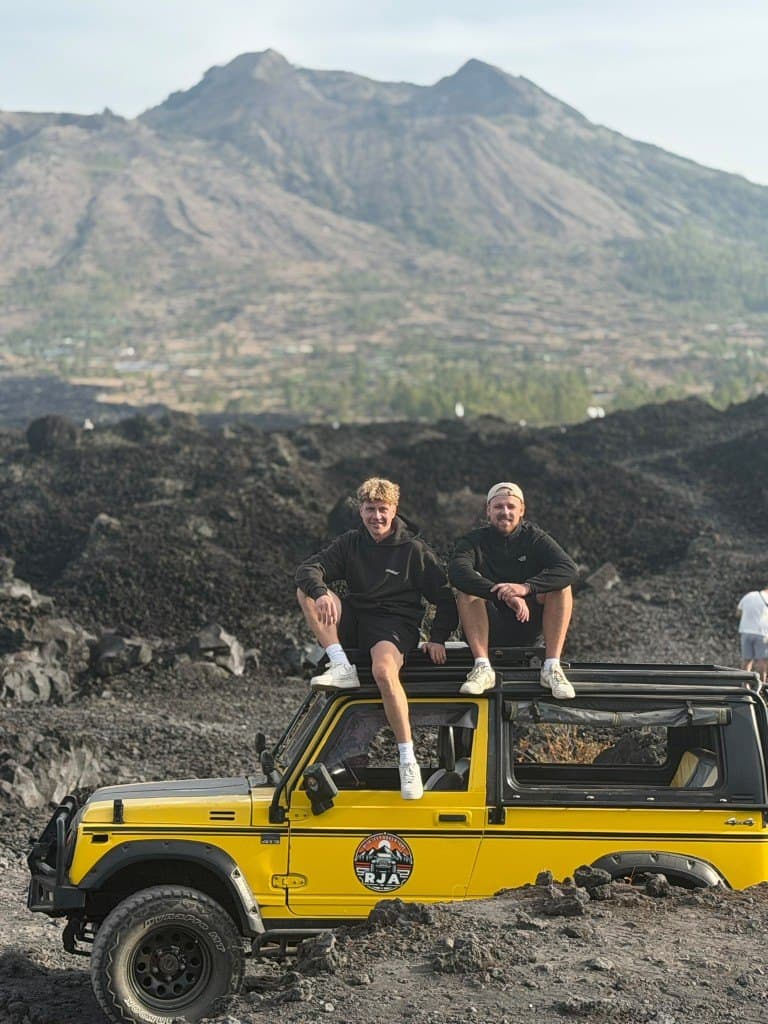 バトゥール山のふもと、黒い溶岩台地で黄色いジープの屋根に座る2人のゲスト