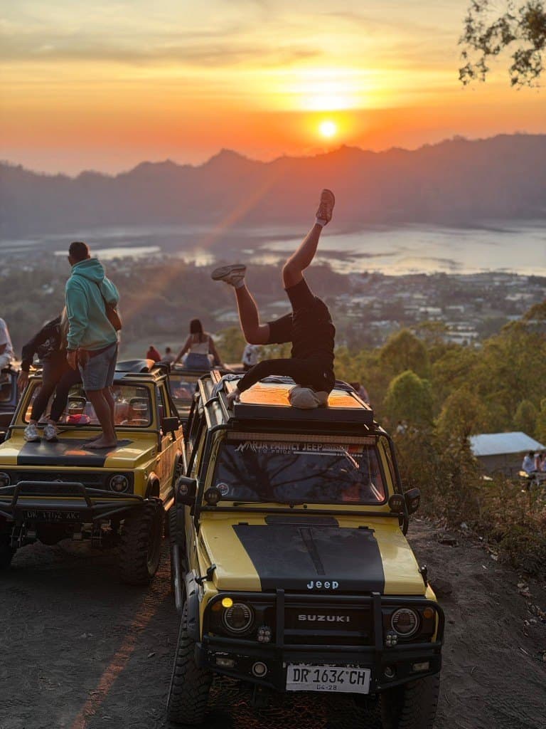 A guest doing a handstand on a jeep roof as the sun rises over the Batur caldera