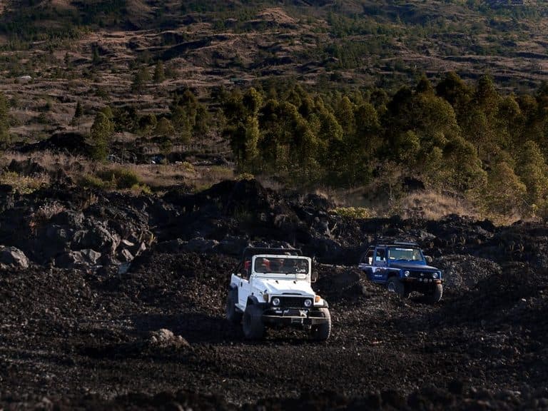 A white and a blue 4×4 crossing the black lava field below Mount Batur on the Kintamani jeep route
