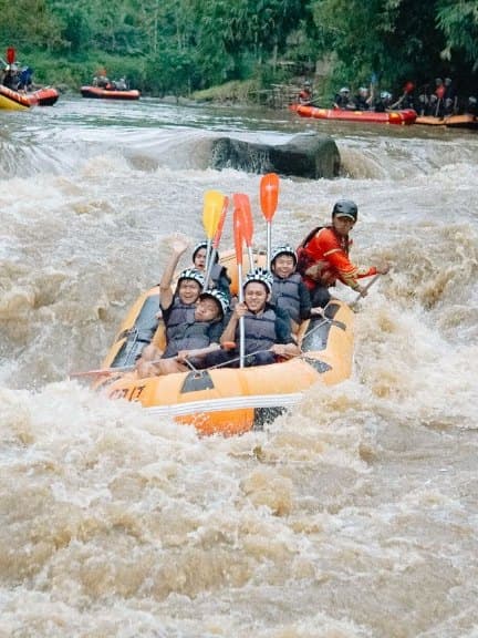 Guests in helmets and life jackets waving from a raft in a rapid