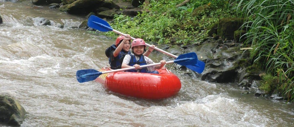 Two guests sharing a red tube and blue paddles on the Wos River
