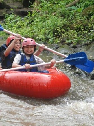 Two guests in helmets and life jackets on one red tube