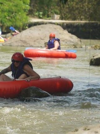 A guest on a red tube in the foreground, with more tubers behind on the river